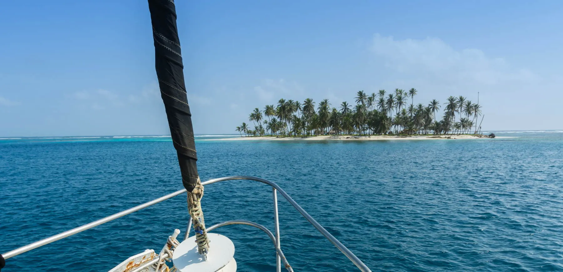View from the bow of the sailboat approaching a palm island in San Blas